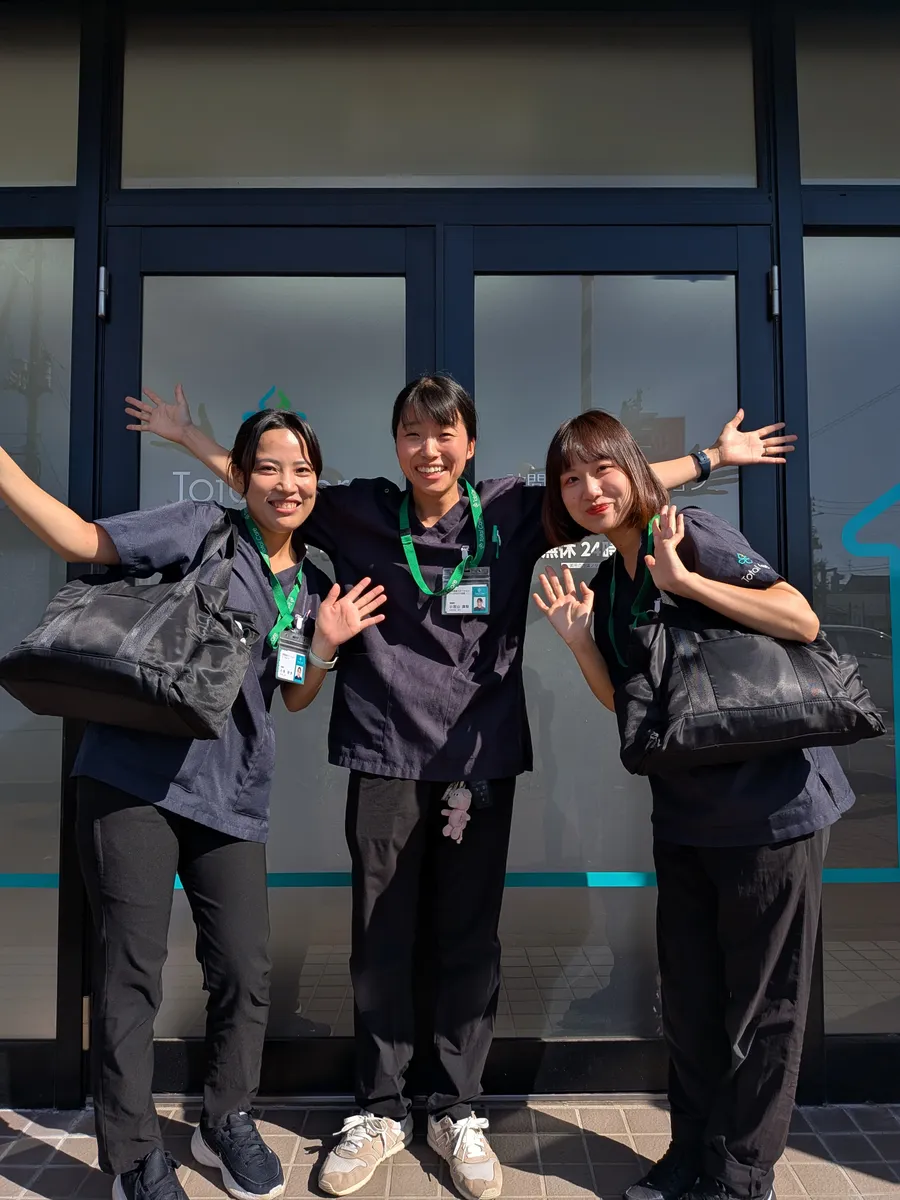 ステーションの入口で、3人の看護師が両手を広げて笑う