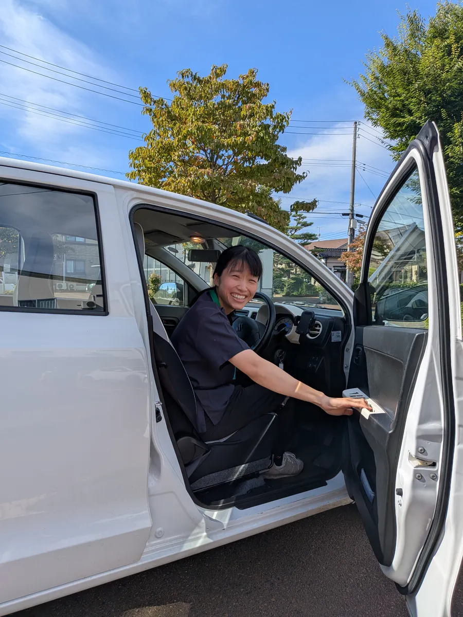 訪問車の運転席から笑顔を見せる看護師