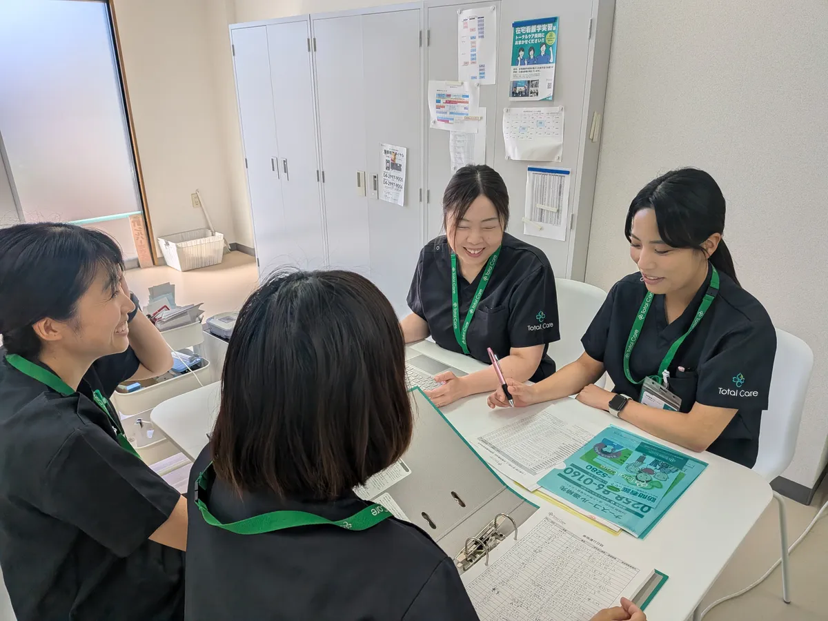 ステーションで、パソコンと書類を囲んで話し合う看護師たち