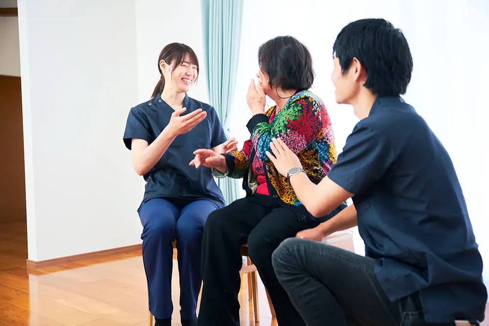 患者さん・ご家族と談笑する看護師。3人が椅子に座って明るく語り合っている様子