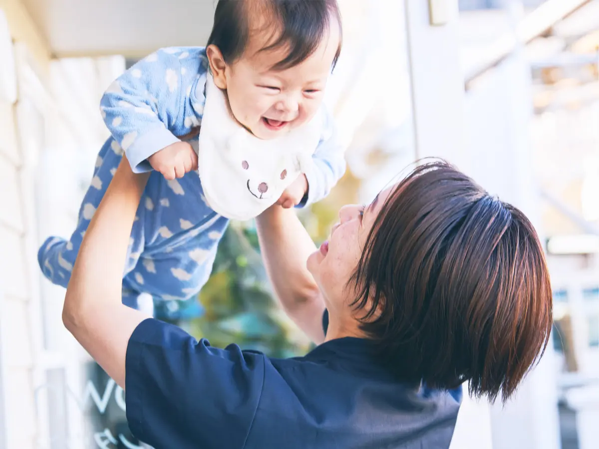 看護師が赤ちゃんを高く抱き上げ、赤ちゃんが笑っている様子