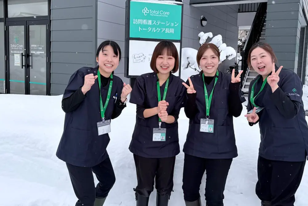 雪の中、トータルケア長岡の前に並ぶ4人の看護師