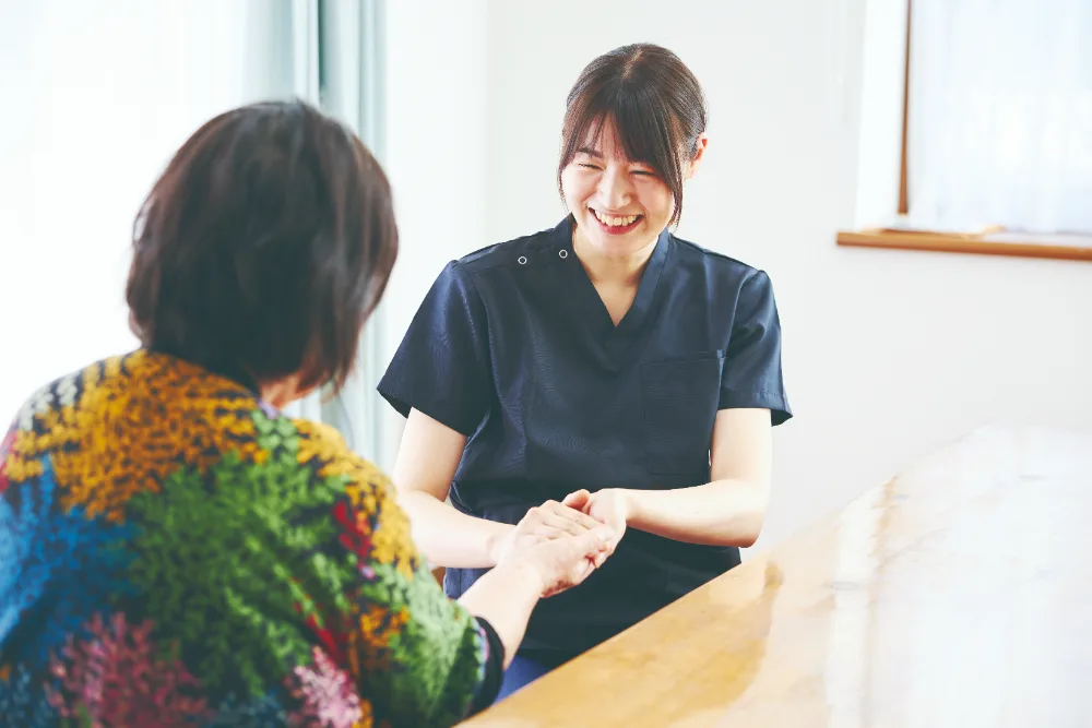 患者様の手を取り、笑顔で話を聞く看護師
